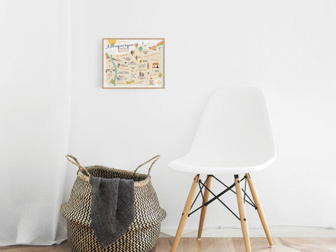 A minimalist room features a white chair, woven basket, and the Onderkast Studio Albuquerque Map Art Print framed on a white wall. Light wood floors and neutral tones add subtle Southwest charm to the decor.