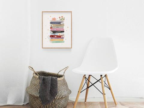 A woven basket with a gray blanket sits beside a modern white chair. Above, the TS Book Stack Art Print by Onderkast Studio hangs on a white wall, bringing Swiftie flair to this minimalistic space.