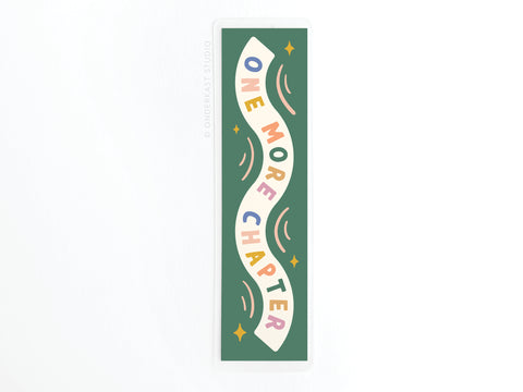The One More Chapter Laminated Bookmark by Onderkast Studio features green laminate, colorful wavy ONE MORE CHAPTER text, small stars, and curved lines—perfect for avid readers.
