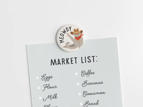 The Meowdy Button Magnet by Onderkast Studio features a cowboy cat saying “MEOWDY.” Perfect for cat lovers, this round magnet holds notes or lists—like eggs, flour, milk, coffee, bananas, cinnamon, and bread—on your fridge.