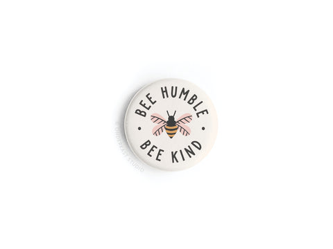 The Bee Humble Bee Kind Button Magnet by Onderkast Studio features a whimsical bee at its center, surrounded by the phrase “Bee Humble Bee Kind” on a white background—an ideal addition to any collection.