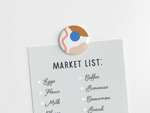 The Abstract No. 2 Button Magnet by Onderkast Studio holds a MARKET LIST with handwritten items such as eggs, flour, milk, coffee, bananas, cinnamon, and bread. This vibrantly printed round magnet is discontinued.