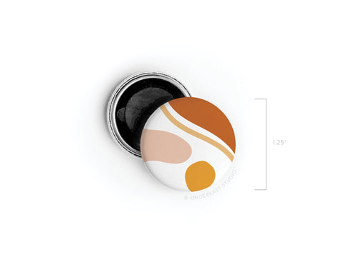 The Abstract No. 5 Button Magnet by Onderkast Studio (now discontinued) features vibrant orange, mustard yellow, white, and beige abstract shapes on a 1.25-inch round magnet, shown next to its open backing.
