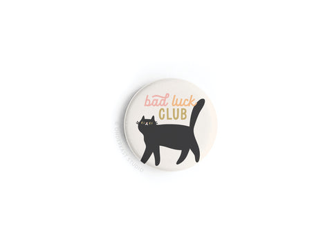 The Bad Luck Club Button Magnet by Onderkast Studio features a black cat illustration and playful Bad Luck Club text on a white background—a fun, quirky accessory for any style enthusiast.