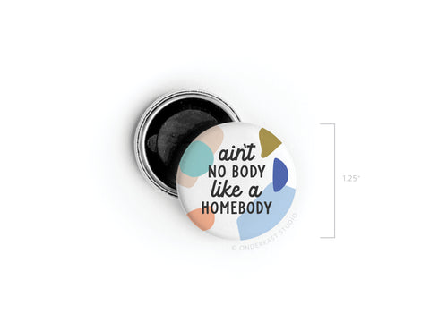 The Ain’t No Body Like a Homebody Button Magnet by Onderkast Studio features colorful abstract shapes and bold black text, sized at 1.25 inches—perfect for introverts and homebodies alike.