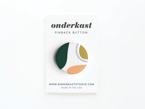 The Abstract No. 1 Pinback Button – DISCONTINUED by Onderkast Studio features bold shapes in green, gold, orange, and white, vibrantly printed and displayed on a branded card with the website and MADE IN THE USA at the bottom.