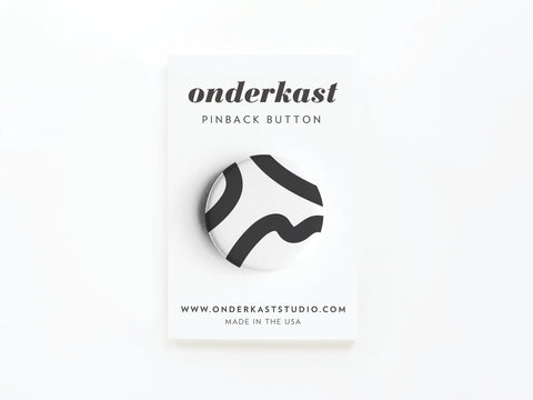 The Abstract No. 3 Pinback Button – DISCONTINUED by Onderkast Studio features a black and white abstract design, is mounted on a white onderkast PINBACK BUTTON card with onderkaststudio.com, Made in the USA, and printed colors displayed below.