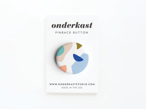 The Abstract No. 4 Pinback Button – DISCONTINUED from Onderkast Studio features vibrant abstract shapes on white, displayed on a card labeled Onderkast Pinback Button with the website and Made in the USA printed below.