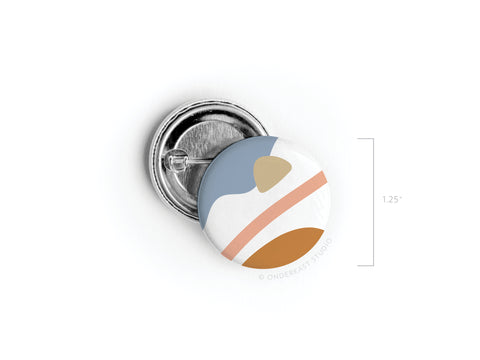 The Onderkast Studio Abstract No. 6 Pinback Button (DISCONTINUED) is a 1.25-inch round button featuring a vibrant abstract design in blue, white, tan, and orange, shown open to reveal its pin mechanism.