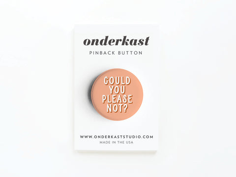 The Could You Please Not Pinback Button by Onderkast Studio is a peach-colored button with printed text, attached to a white card showing the brand, website, and MADE IN THE USA. This item is discontinued.