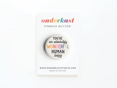 A vibrantly printed Absolutely Wonderful Human Being Pinback Button by Onderkast Studio is displayed on a card featuring the brand name, website, and “Made in the USA” at the bottom.