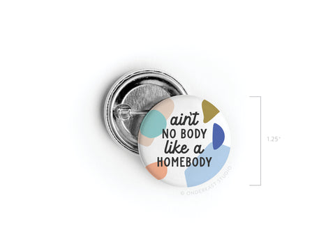 Onderkast Studio’s “Ain’t No Body Like a Homebody” Pinback Button features bold black text and abstract shapes on a crisp white 1.25 round button—the perfect vibrant accessory for introverts.