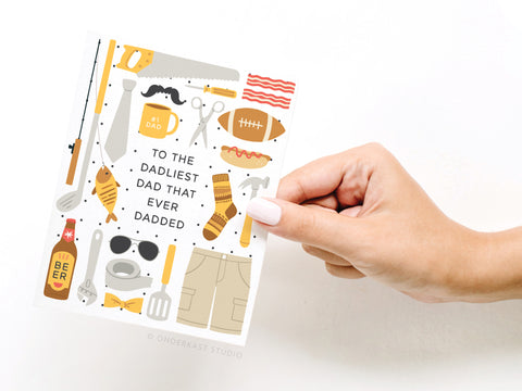 A hand holds the Onderkast Studio “To the Dadliest Dad That Ever Dadded” Greeting Card, decorated with dad-themed illustrations. Printed in the USA.