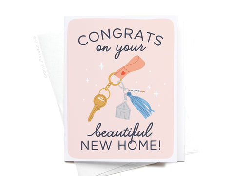 The Congrats on Your Beautiful New Home Keychain Greeting Card by Onderkast Studio features a hand holding keys with a new home keychain and the message “Congrats on your beautiful new home!” on a soft pink background, with envelope included.