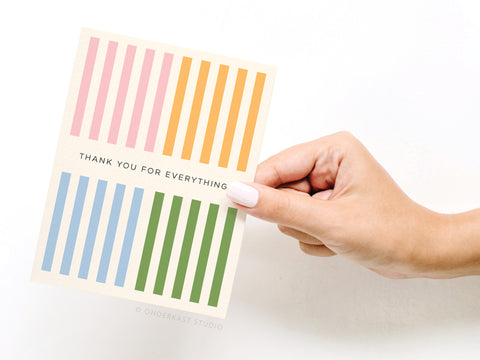 A hand with light pink nail polish holds the Onderkast Studio Thank You for Everything Greeting Card, which features colorful vertical stripes and the message “THANK YOU FOR EVERYTHING” in the center.