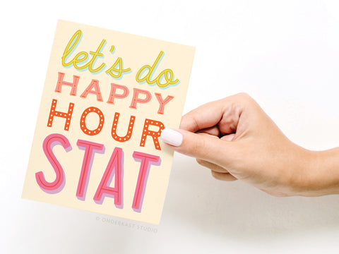 A hand with white nail polish holds the Let’s Do Happy Hour Stat Greeting Card by Onderkast Studio, featuring colorful, playful fonts on a light background for a premium feel.