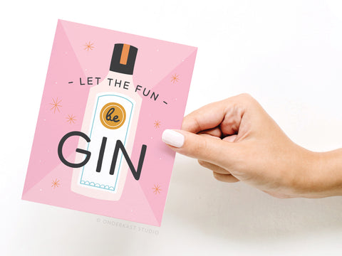 A hand with a light pink manicure holds Onderkast Studio’s Let the Fun Be Gin Greeting Card, featuring an illustrated gin bottle, playful stars, and the phrase Let the fun beGIN—perfect for any celebration.