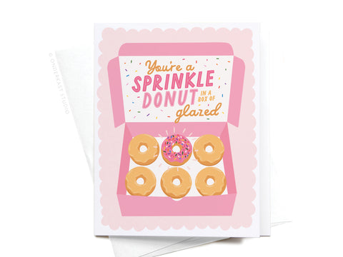 Onderkast Studio’s You’re a Sprinkle Donut Greeting Card features a pink box with five glazed donuts and one sprinkled donut, plus the lid message: Youre a sprinkle donut in a box of glazed. A sweet way to share love!.