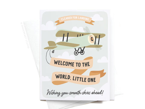 The Welcome to the World Little One Greeting Card by Onderkast Studio features a vintage airplane flying among clouds with banners reading “Cleared for Landing,” “Welcome to the World, Little One,” and “Wishing you smooth skies ahead!”.