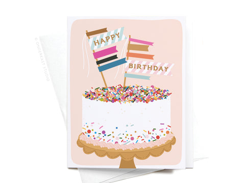 The Happy Birthday Sprinkle Cake Greeting Card by Onderkast Studio features a sprinkle cake with two Happy Birthday flags on a decorative stand, set against a light pink background for an elegant touch.
