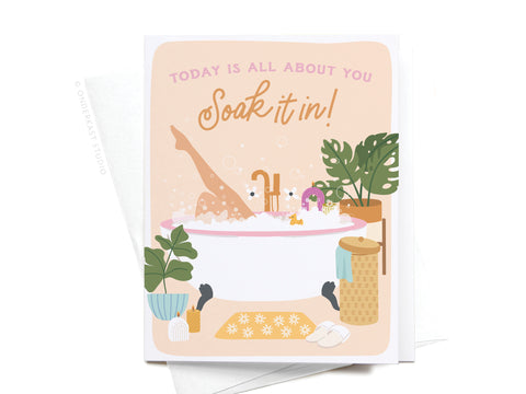 The Soak It In Bubble Bath Greeting Card by Onderkast Studio features a relaxing bath scene with a person in a tub, plants, basket, slippers, and bubbles. Perfect for celebrating self-care. Text on card: Today is all about you. Soak it in!.