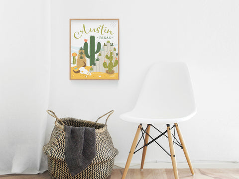 A minimalist room features a white chair, woven basket, and the Austin Succulent Skyline Art Print by Onderkast Studio—a cactus-themed poster that brings Texas-inspired style to the decor.