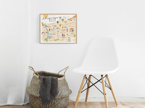 A woven basket and a white chair sit on a wooden floor against a white wall, accented by the colorful Onderkast Studio Albuquerque Map Art Print above them, bringing Southwest charm to the space.