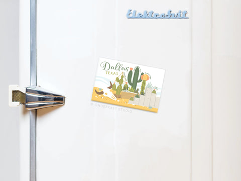 A refrigerator door with a silver handle displays Onderkast Studios Dallas Succulent Skyline Refrigerator Magnet, featuring cacti and desert art. Blue magnets above spell out Elektrobit in a playful style.