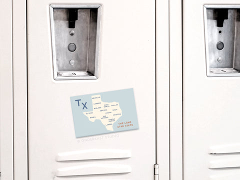 A plain white locker displays the Onderkast Studio Texas Map Refrigerator Magnet, labeled THE LONE STAR STATE in red and highlighting Texas cities—adding state pride to ordinary metallic lockers.