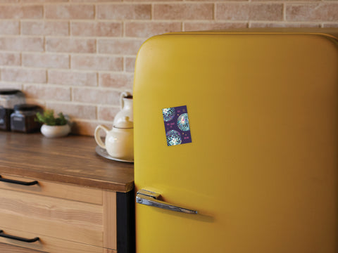 A yellow retro-style refrigerator with the Onderkast Studio All We Have Is Now Disco Balls Refrigerator Magnet on its door stands in a kitchen with wooden countertops, a teapot, jars, and a brick backsplash in the background.