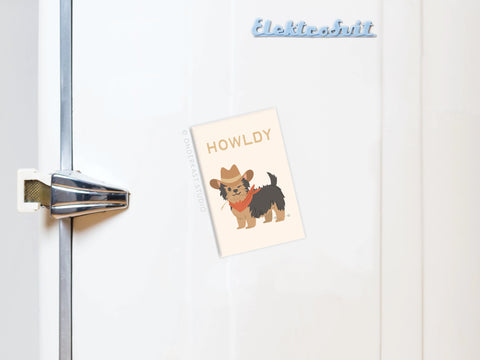 The Onderkast Studio Howldy Dog Refrigerator Magnet, showing a pup in a cowboy hat and red bandana with the caption HOWLDY, is displayed on a white fridge with a retro handle.
