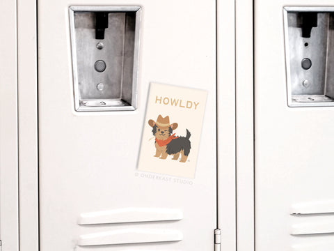 A white locker displays the Onderkast Studio Howldy Dog Refrigerator Magnet: a whimsical magnet featuring a small dog in a cowboy hat and bandana, with the word HOWLDY above the illustrated pup.
