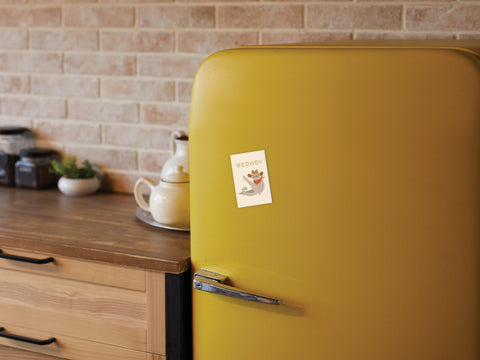 A yellow retro fridge adorned with the Onderkast Studio Meowdy Cat Refrigerator Magnet is set in a kitchen featuring a wooden counter, teapot, and jars against a brick wall.