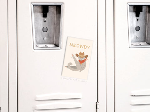 A white locker with a postcard showing a cartoon cat in a cowboy hat and bandana reading MEOWDY—the perfect place to display your Onderkast Studio Meowdy Cat Refrigerator Magnet for extra feline flair.