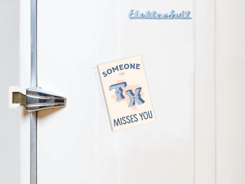 A white fridge with a vintage handle displays the Onderkast Studio Someone in TX Misses You magnet, featuring bold, stylized TX letters. Elektrobit is shown in blue at the top of the refrigerator.
