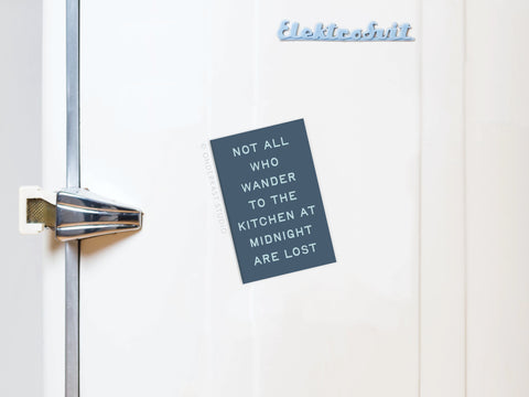 A white vintage refrigerator with a metallic handle displays the Onderkast Studio Not All Who Wander to the Kitchen magnet.