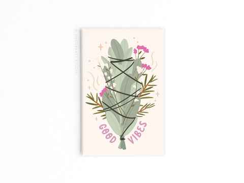 Onderkast Studios Good Vibes Smudge Stick Refrigerator Magnet features a smudge stick tied with black string, adorned with pink flowers and green sprigs. GOOD VIBES appears in purple below this charming magnet.