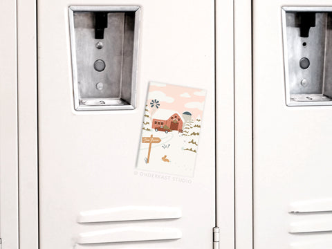 A white locker with rustic charm is decorated with Onderkast Studios Christmas Tree Farm Refrigerator Magnet, which features a festive red barn, windmill, and snowy landscape.