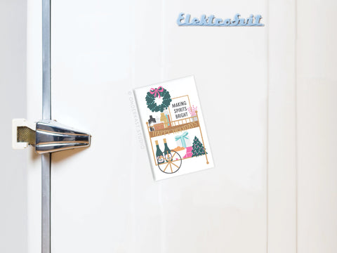 A festive holiday card with Making Spirits Bright and cheerful illustrations is held on a fridge by the Onderkast Studio Making Spirits Bright Bar Cart Refrigerator Magnet, featuring the blue Elektrobrüt logo under a silver latch.