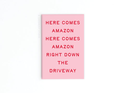The Here Comes Amazon Refrigerator Magnet by Onderkast Studio features pink with red text—HERE COMES AMAZON HERE COMES AMAZON RIGHT DOWN THE DRIVEWAY—a fun addition to your fridge or shopping list, shown on a plain white background.