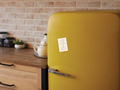 A yellow retro fridge in the kitchen displays the Onderkast Studio Taylor’s Version Refrigerator Magnet, featuring a Swifties-themed note: “In this house, we listen to Taylors Version.”.