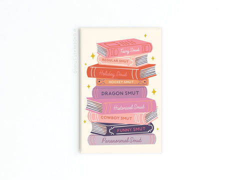 Onderkast Studio’s Smut Book Stack Refrigerator Magnet features a pastel stack of books, each spine labeled with a different romance genre—perfect for any naughty bookworm’s fridge.