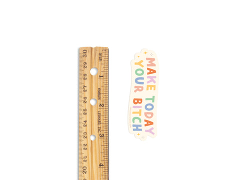 A wooden ruler stands next to the Onderkast Studio Make Today Your Bitch Sticker, a colorful vinyl design printed in the USA with playful uppercase lettering, set against a clean white background.