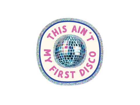 The “This Ain’t My First Disco Glitter Sticker” by Onderkast Studio features bold pink and purple text circling a disco ball on a cream background with a holographic border. Made from weatherproof vinyl.