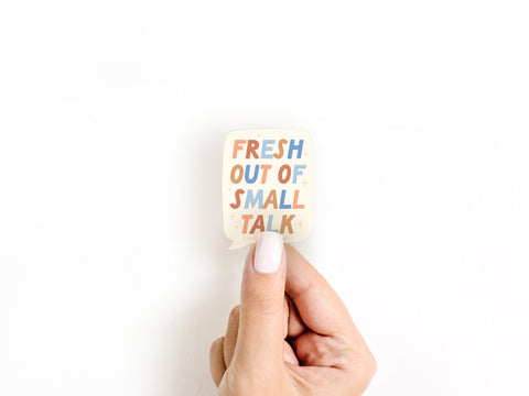 A hand with light nail polish holds the Fresh Out Of Small Talk Sticker by Onderkast Studio. This colorful, speech bubble-shaped vinyl sticker is perfect for introverts to express themselves without saying a word.