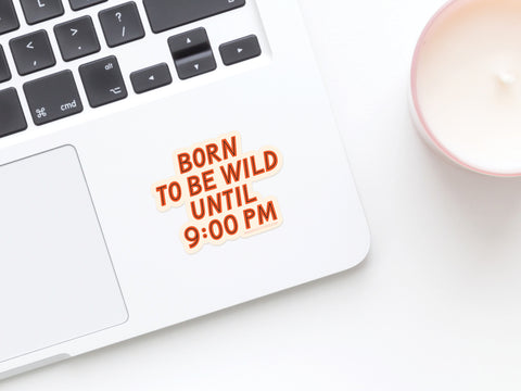 A laptop with an Onderkast Studio Born To Be Wild Sticker, made from weatherproof vinyl, sits beside a pink candle on a white surface.