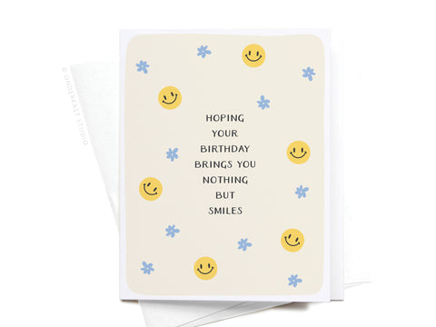 The Nothing But Smiles Greeting Card by Onderkast Studio features the message Hoping your birthday brings you nothing but smiles with yellow smiley faces and blue flowers on a beige background—a cheerful card for any celebration.