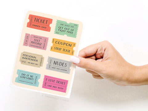 A hand holds Onderkast Studio’s Love Coupons Greeting Card, featuring playful vouchers like Dinner Date, Foot Massage, Strip Tease, Nudes, and more—perfect for gifting someone special!.