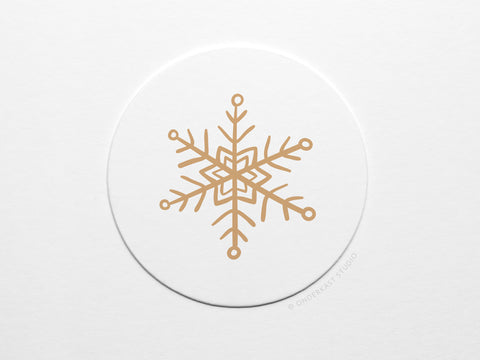The Snowflake Coaster Set by Onderkast Studio features a gold geometric snowflake on a white circle, offering a minimalist and elegant winter design—ideal for handmade letterpress coasters made from durable pulp board.