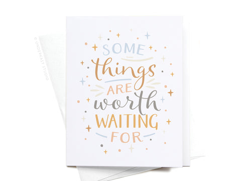 The Onderkast Studio Some Things Are Worth Waiting For Greeting Card features pastel stars and blue, gold, and grey text in vibrant print, paired with a white envelope for a premium touch.